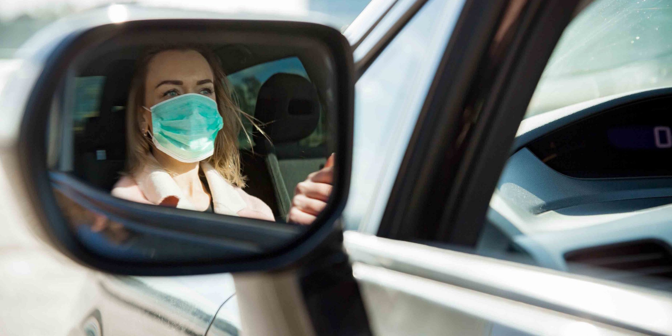 Woman in protective mask driving a car on road.